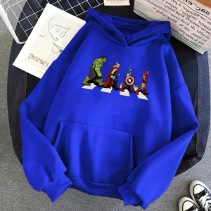 Pull marvel style sweat avec poche et chaud posé sur une moquette grise avec une paire de chaussures en bas à droite et un magazine à gauche